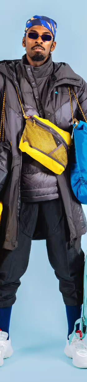 A stylish man wearing many layers of Klattermusen clothing including numerous jackets and bags