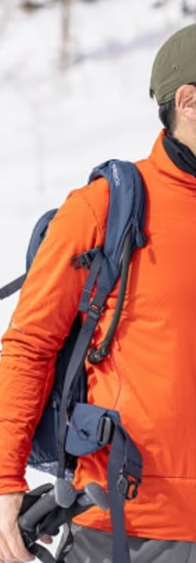 A man looking off in the distance on a snowy mountain wearing an orange Norrona jacket