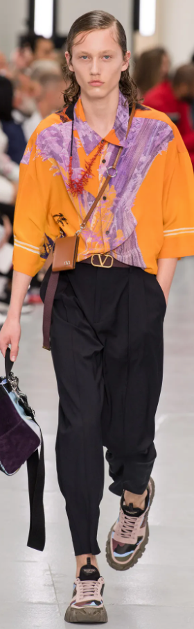 A person wearing an orange Valentino button up, black pants and colorful sneakers