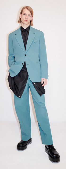 A man wearing a aqua blue suit with a blue jacket underneath along with black loafers