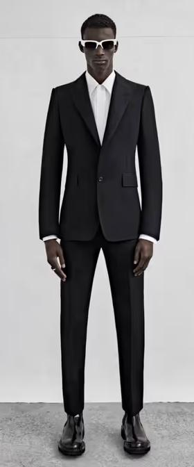 A man wearing a black Alexander McQueen suit with black and white sunglasses